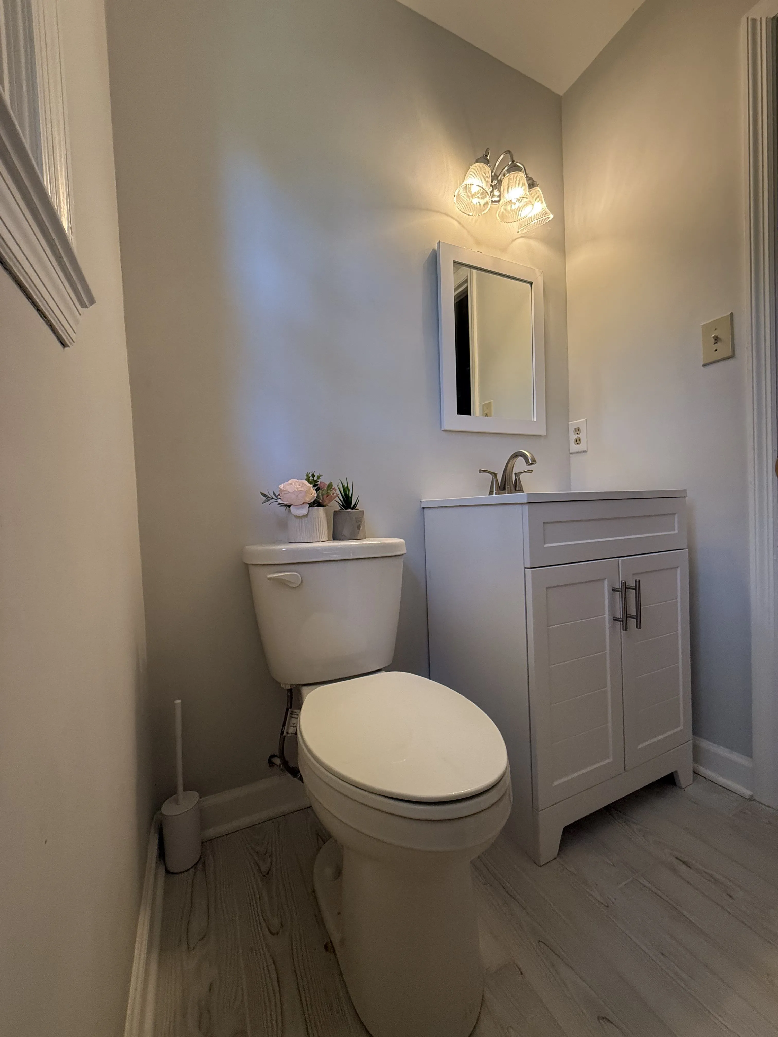A finished bathroom remodel by Carolina Pro Restoration with a new vanity, mirror, light fixture, and waterproof plank flooring